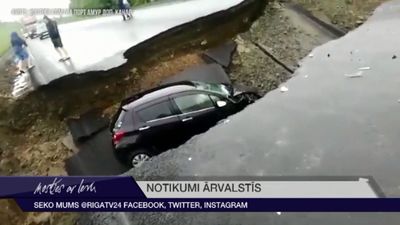 Krievijā automašīna uz šosejas iekrīt lietusgāžu izskalotā bedrē